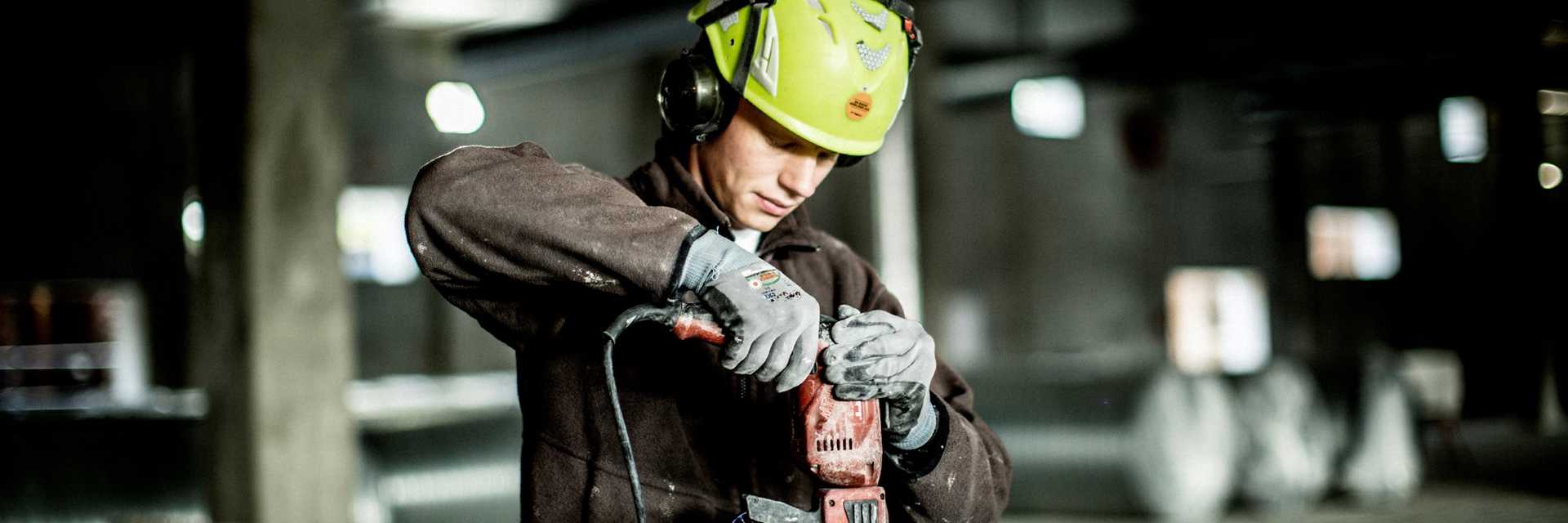 Mand der er ved at bore i metal. Han er udstyret med hjelm og arbejdstøj.